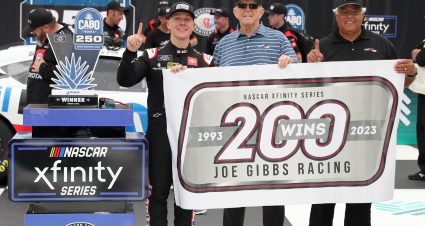 BROOKLYN, MICHIGAN - AUGUST 05: (L-R) John Hunter Nemechek, driver of the #20 Mobil 1 Toyota, JGR team owner and Hall of Famer, Joe Gibbs and Steve deSouza, EVP NASCAR Xfinity Series/Development pose with a flag in honor of Joe Gibbs Racing's 200th NASCAR Xfinity Series win, in victory lane after winning the NASCAR Xfinity Series Cabo Wabo 250 at Michigan International Speedway on August 05, 2023 in Brooklyn, Michigan. (Photo by Meg Oliphant/Getty Images) | Getty Images