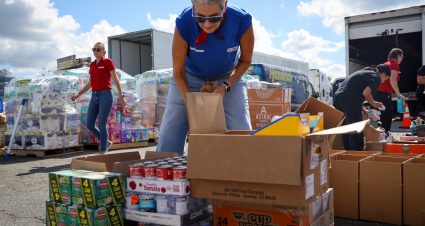 Cms Team Member Packing A Box Of Donated Canned Goods.