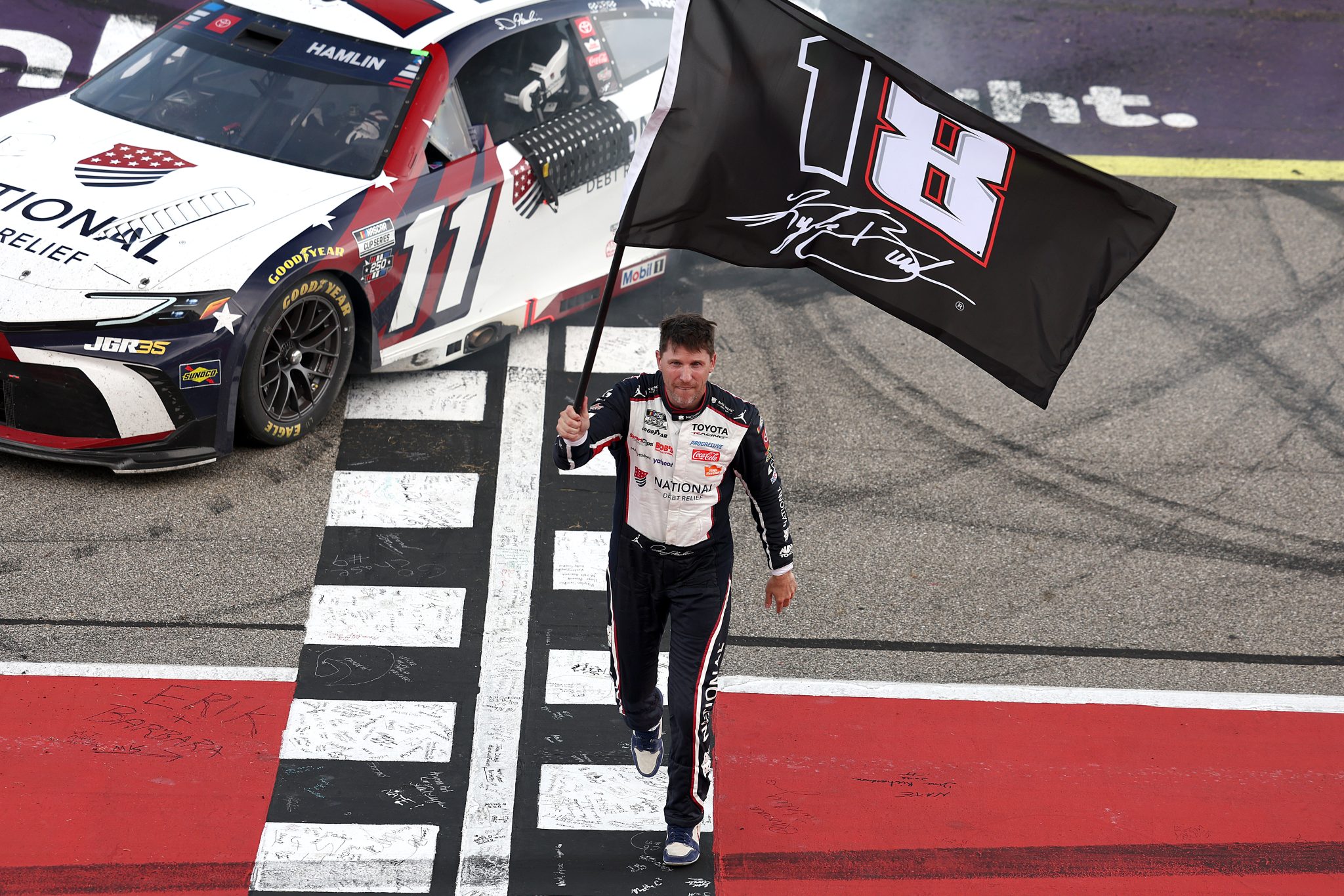 BROOKLYN, MICHIGAN - JUNE 07: Denny Hamlin, driver of the #11 National Debt Relief Toyota, waves an 18 - 8 flag in honor of the late Kyle Busch after winning the NASCAR Cup Series FireKeepers Casino 400 at Michigan International Speedway on June 07, 2026 in Brooklyn, Michigan. (Photo by Brett Farmer/Getty Images) | Getty Images